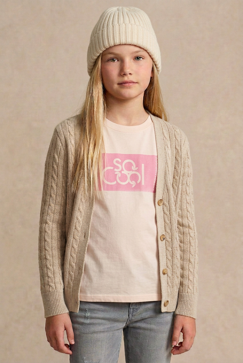 Blonde model in the pale pink logo tee with an oatmeal cardigan and cream beanie