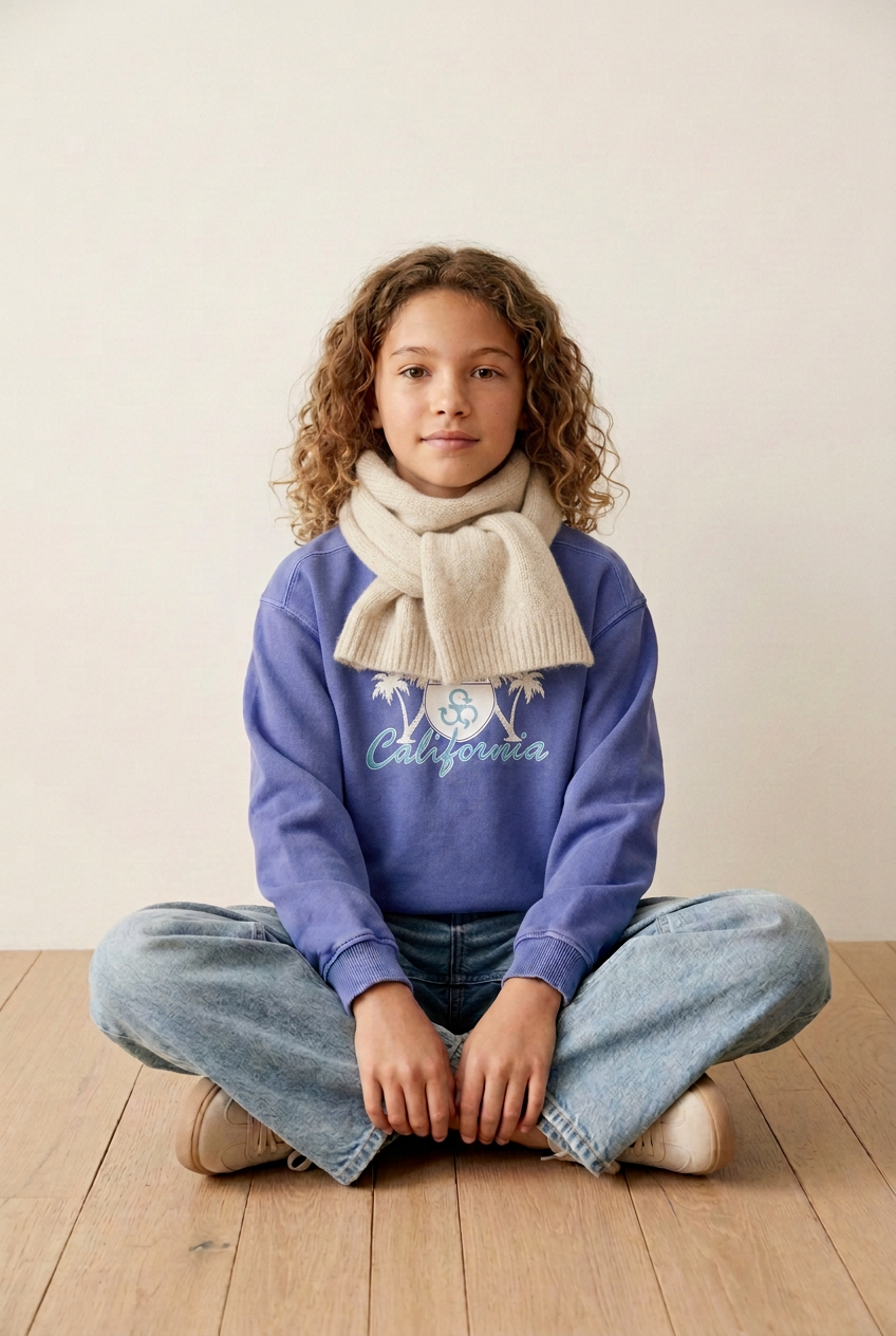 Tween model with a tied cream scarf positioned to cover the website lettering